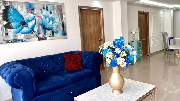 A modern living room with a blue sofa, a white marble coffee table, and a vase of flowers. - hostal costa caribe (Barranquilla)