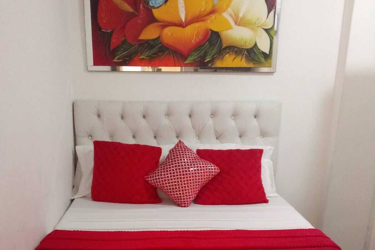 Una cama con una manta roja, dos almohadas rojas y un cabecero blanco.