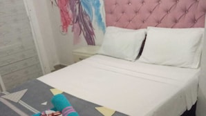 A neatly made bed with a pink tufted headboard, white pillows, and a grey bedspread with geometric patterns and the word "love". - hostal costa caribe (Barranquilla)