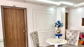 A room with two upholstered chairs, a round table, a wooden door, and a wall-mounted vase with flowers. - hostal costa caribe (Barranquilla)