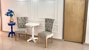 A room with two grey upholstered chairs, a small round table, and a blue side table with a vase of flowers. A closed door is visible in the background. - hostal costa caribe (Barranquilla)