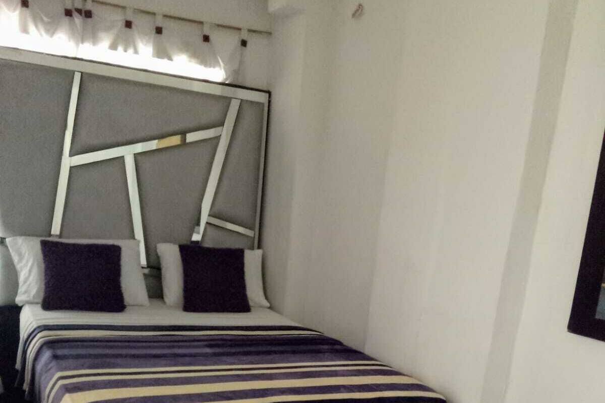 Una habitación de hotel con dos camas, cada una con ropa de cama a rayas, un cabecero con diseño geométrico y una pared blanca.