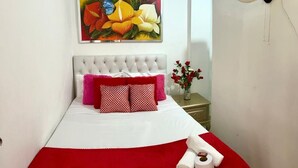 A neatly made bed with a white and red bedspread, a tufted headboard, and a painting of flowers above it. - hostal costa caribe (Barranquilla)