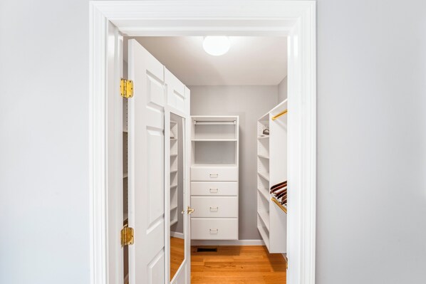 A narrow walk-through closet with white shelving and drawers, a wooden floor, and a white door with a brass handle. - Private Guest House Near the Beach • 1BR / 1.5BA (Old Lyme)