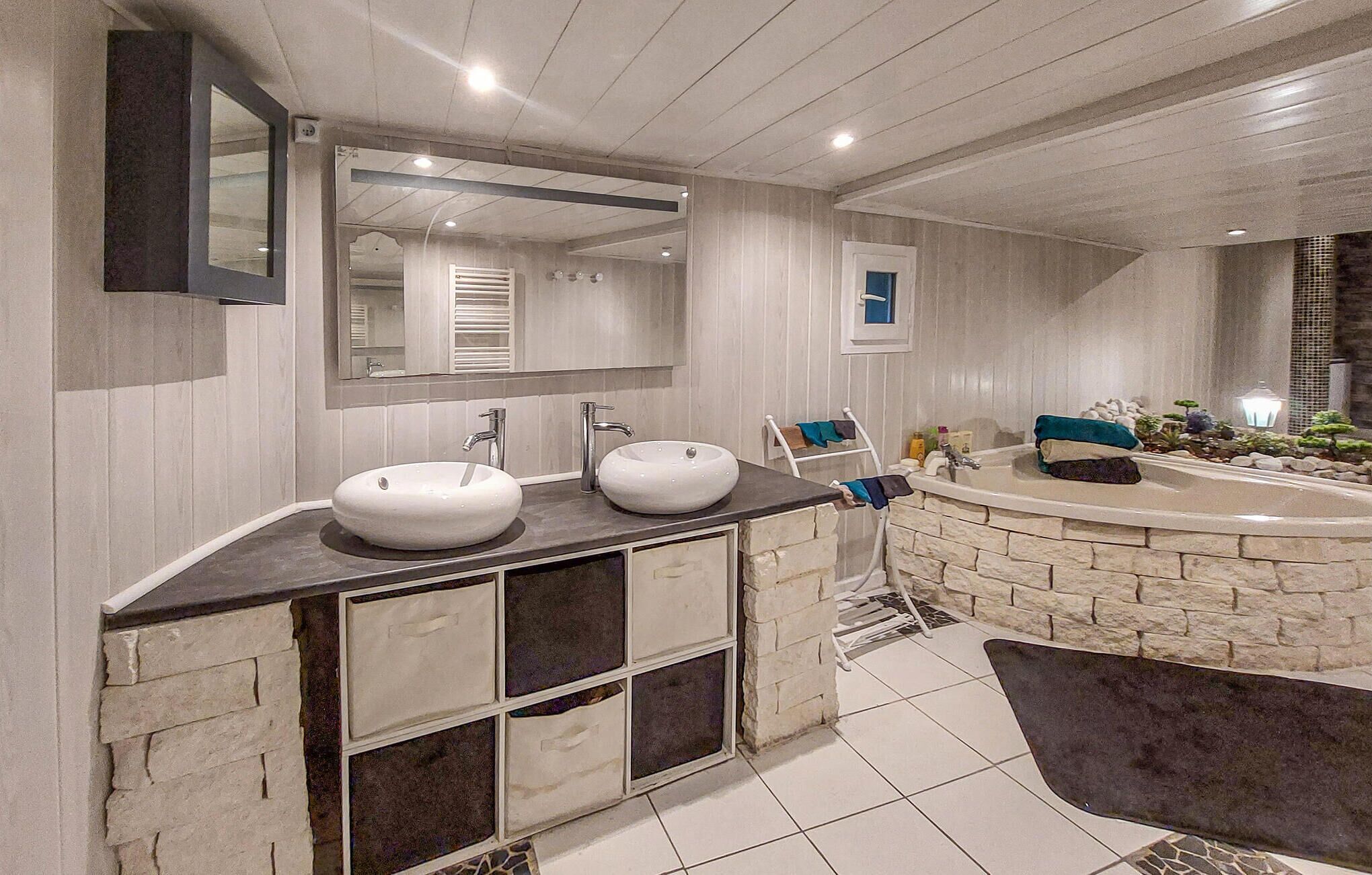 A modern bathroom with two sinks, a large mirror, and a stone accent wall.