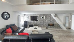 A modern living room with a black leather sofa, a white coffee table, and a stone wall. - Gorgeous home in Villars (Villars)