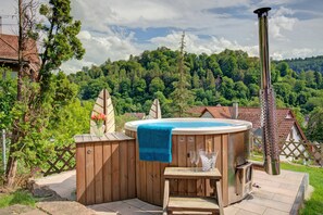 A hot tub with a wooden deck and a blue towel, surrounded by a wooden fence and a view of a forested hillside.