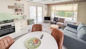 Una cocina moderna con estufa a gas, horno y espacio para café. Hay un comedor con mesa y sillas, y una sala de estar con sofá y sillones.