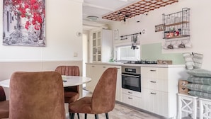 Una cocina moderna con armarios blancos, horno empotrado y una zona de comedor con sillas marrones.