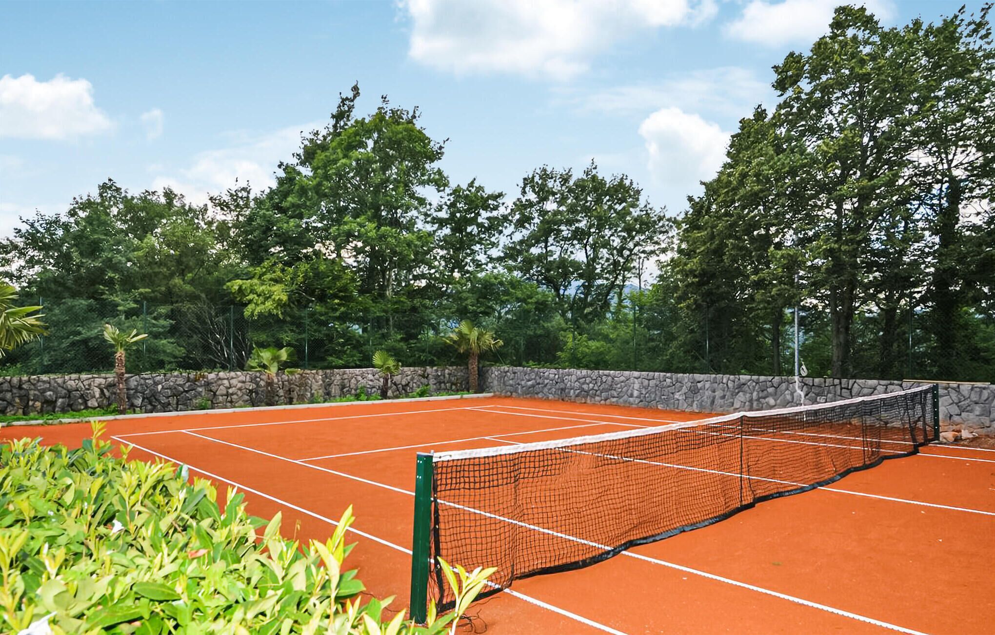 A tennis court with a stone wall and trees in the background.