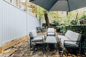Relax on the patio with a sofa and two chairs, shaded by a large umbrella.