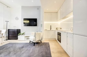 Relax in this stylish living space featuring a comfortable sofa, flat-screen TV, and modern kitchen with oven and dishwasher.
