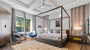 Ein modernes Schlafzimmer mit einem Himmelbett, einem großen, flauschigen Teppich, einem Schaukelstuhl, einem Nachttisch mit Lampe und einer Pendelleuchte.