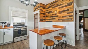 A kitchen with a wooden accent wall, a stainless steel oven, a wooden countertop, and bar stools. - Emerald Square I 4 King Beds I 3 Bath I Loft Area (Lansing)