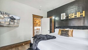 A bedroom with a large bed, a wooden headboard, and a wall-mounted shelf with a sign. - Emerald Square I 4 King Beds I 3 Bath I Loft Area (Lansing)