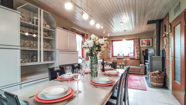 Comedor con una mesa larga dispuesta para seis comensales, flanqueado por vitrinas de vidrio y una pared de ladrillo.