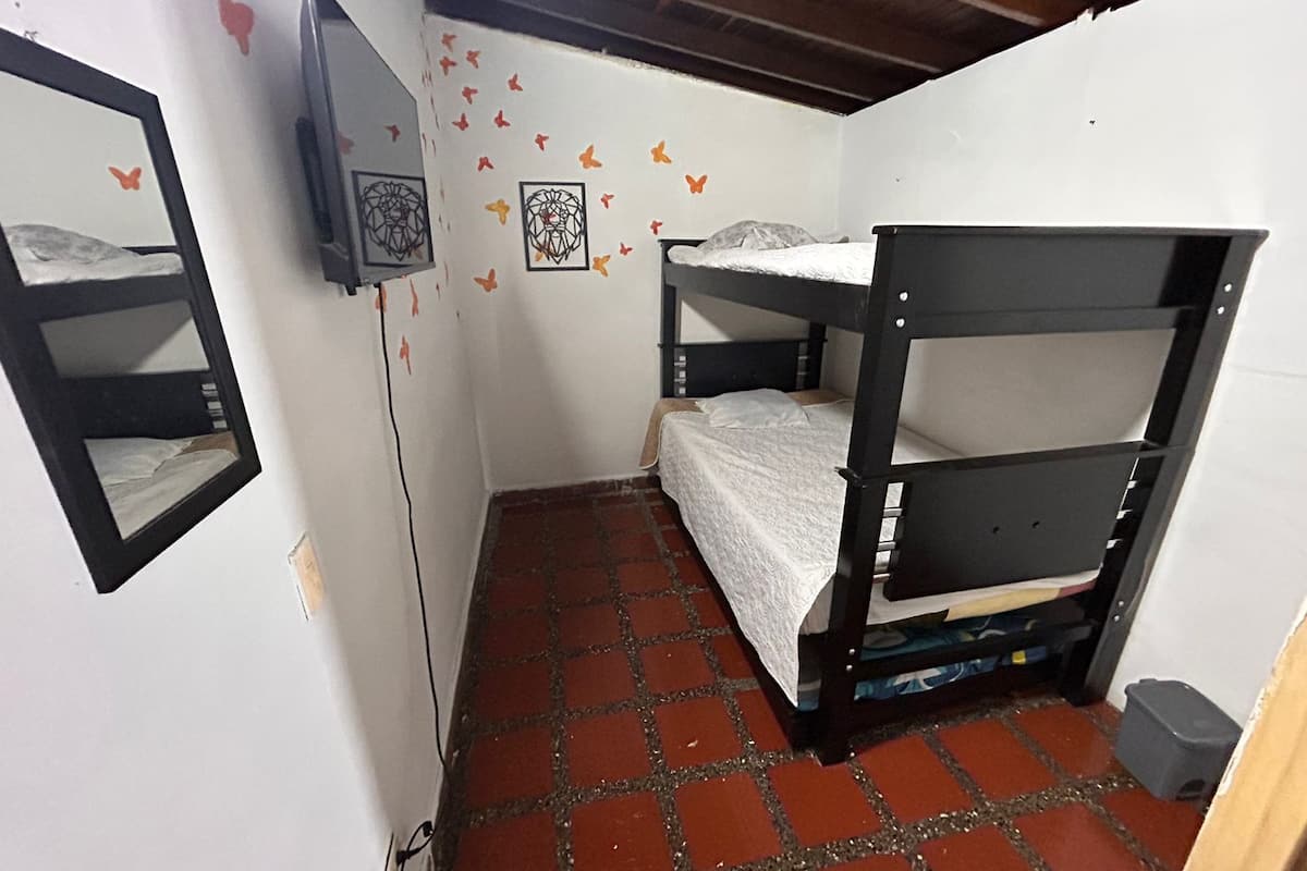 Una habitación pequeña y funcional con una cama litera, un televisor y una pared decorada con pegatinas de mariposas.