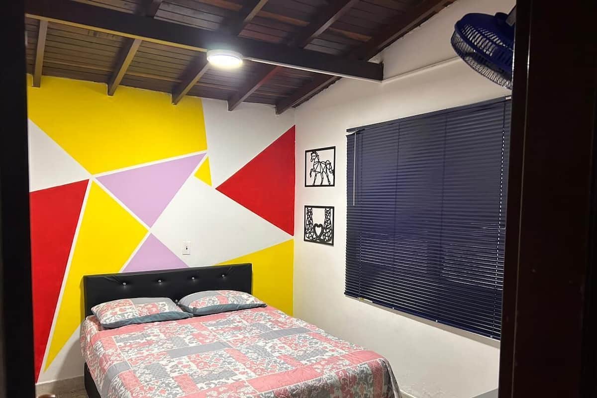 Un dormitorio con cama, una ventana con persianas y una pared con diseños geométricos.