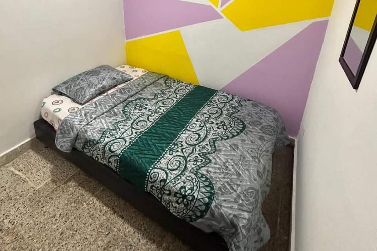 Un dormitorio pequeño con una cama, una pared con diseños geométricos y un techo con vigas de madera.