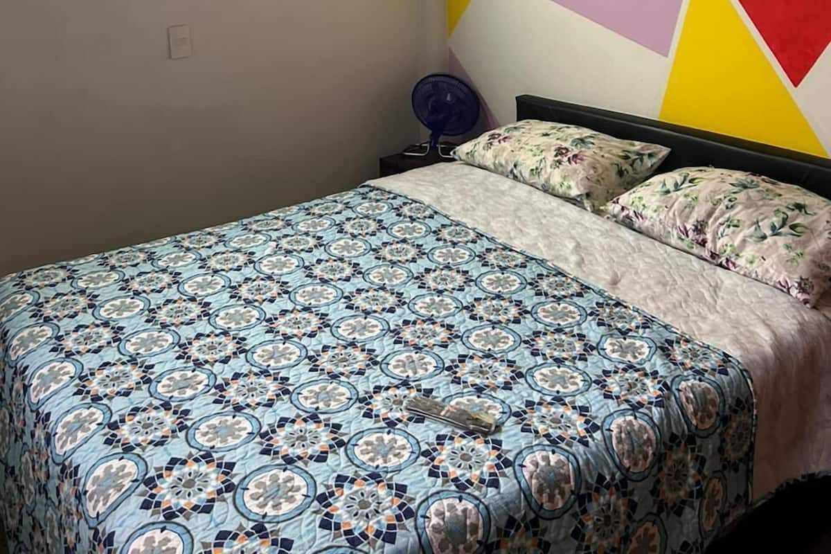 Un dormitorio con una colcha estampada, una pared con arte geométrico y un techo con vigas de madera.