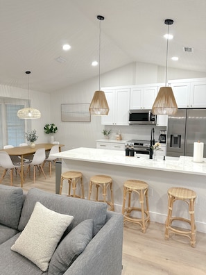Een moderne keuken met witte kasten, een centraal eiland met barstoelen en hanglampen.