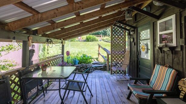 A covered porch with a table and chairs, a wooden deck, and a view of a garden.