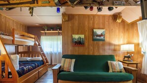 A cozy cabin with a bunk bed, a green sofa, and wooden walls.