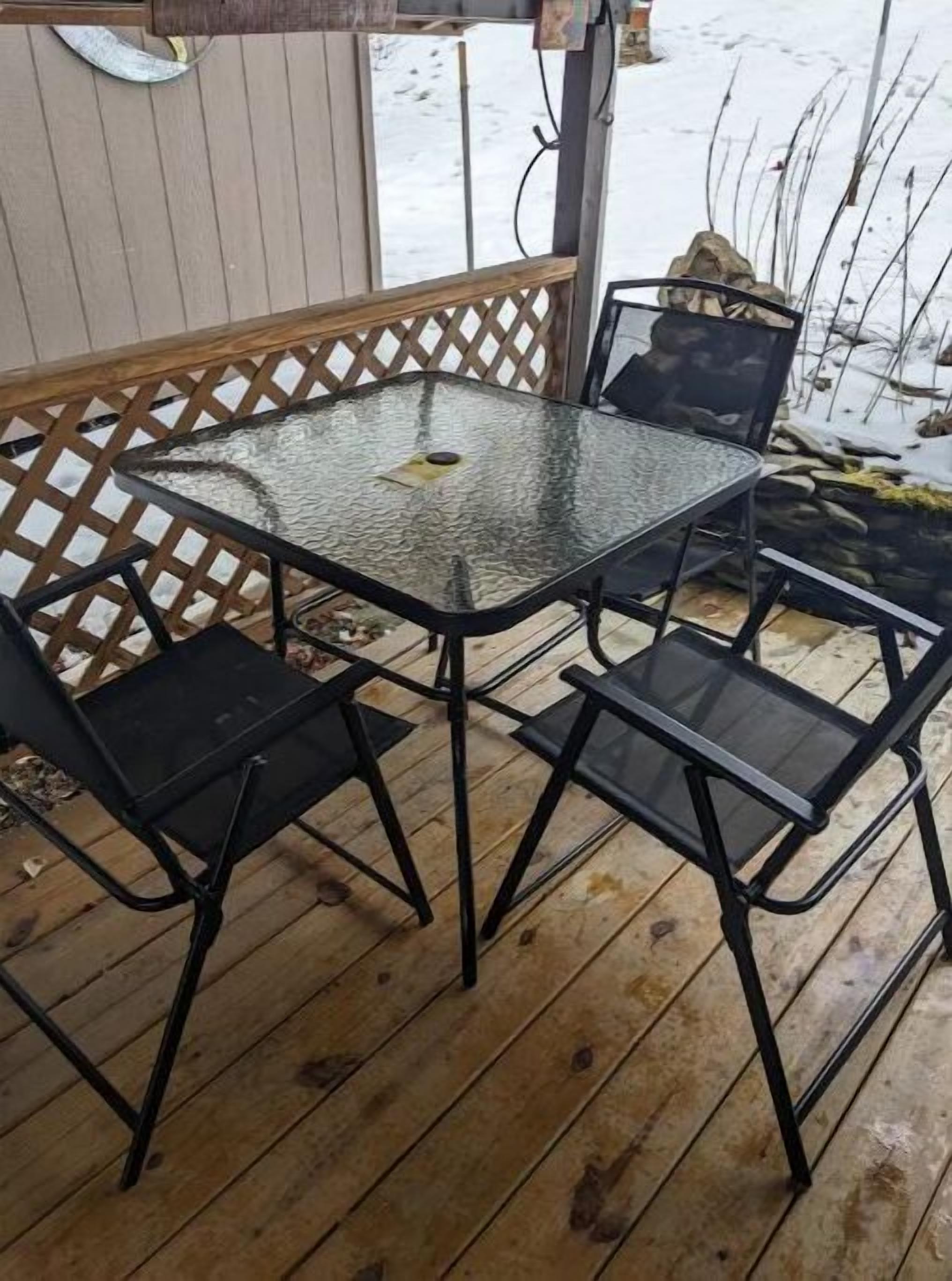 Un tavolo con ripiano in vetro e quattro sedie nere su un pontile di legno.