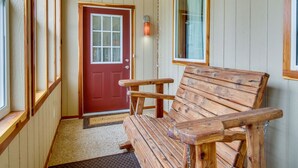 Un banc en bois dans un couloir, avec une porte rouge et une fenêtre.