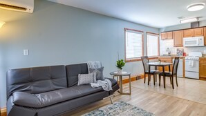 Un salon moderne avec un canapé gris, une petite table ronde avec des chaises et un coin cuisine doté de meubles en bois et d’un four à micro-ondes.