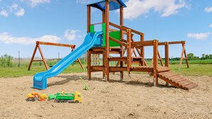 A wooden playground structure with a blue slide and a climbing ladder, set on sandy ground with toys nearby. - Nice home in Jaroslawiec with WiFi (Jaroslawiec)