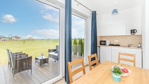 A modern kitchen with white cabinets and a microwave, a wooden dining table with chairs, and a view of a grassy field through large windows. - Nice home in Jaroslawiec with WiFi (Jaroslawiec)