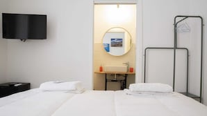 Habitación de hotel con dos camas, televisión, espejo, lavamanos y toallero.