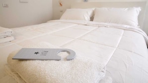 Una cama bien hecha con edredón blanco y almohadas, una toalla pequeña y un llavero con un símbolo de estrella sobre una almohada blanca.