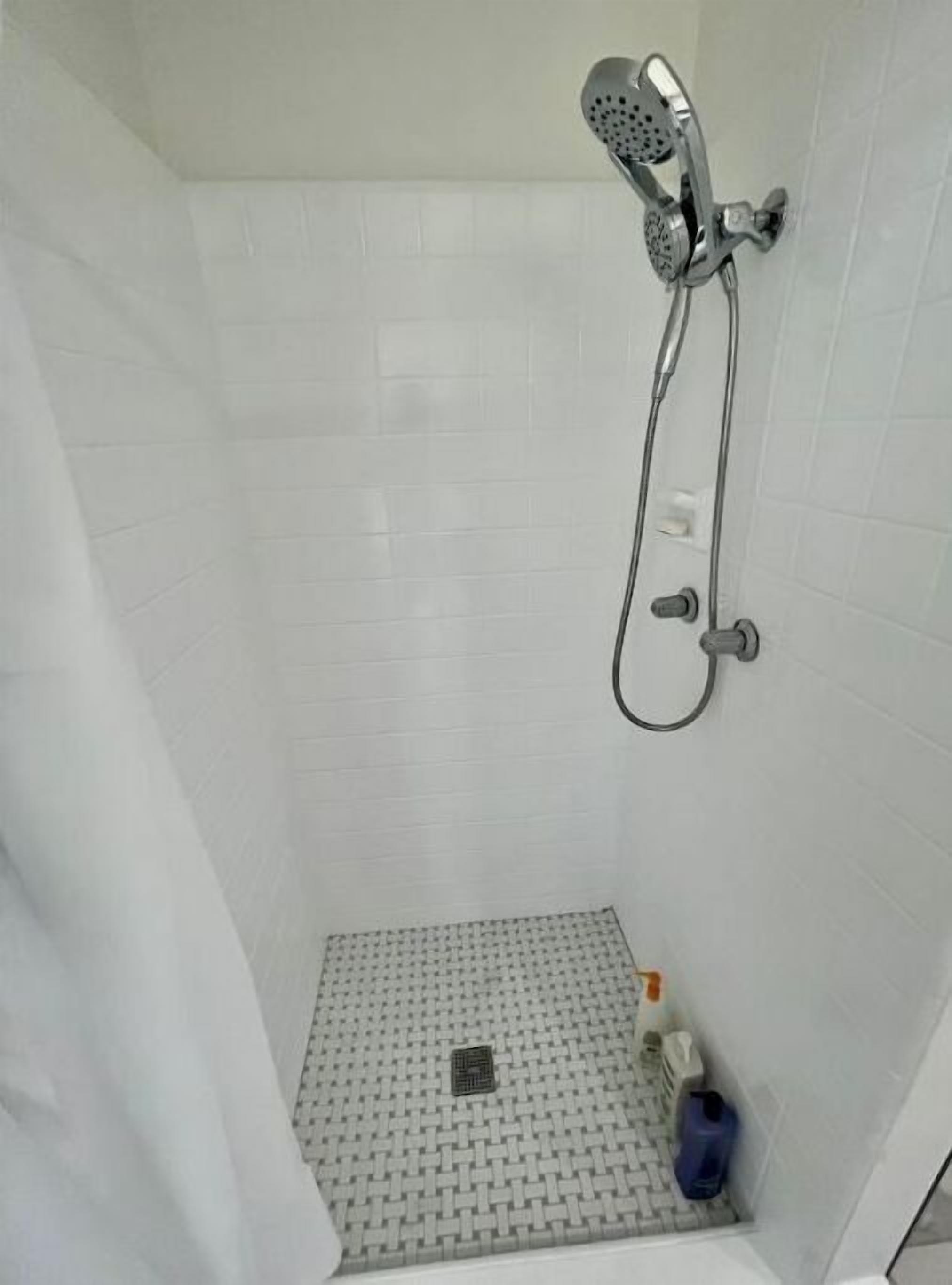 A small, tiled shower area with a handheld showerhead and a drain.