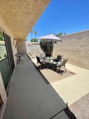 Relax in the serene patio area, surrounded by lush greenery and a pergola, with a table for al fresco dining.