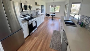 A modern kitchen with stainless steel appliances, a dining area with a table and chairs, and large windows providing natural light. - Relaxing Golf Course, Pool, remodeled sleeps 6 (La Quinta)