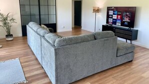A modern living room with a grey sectional sofa, a flat-screen TV, and a sliding glass door. - Relaxing Golf Course, Pool, remodeled sleeps 6 (La Quinta)