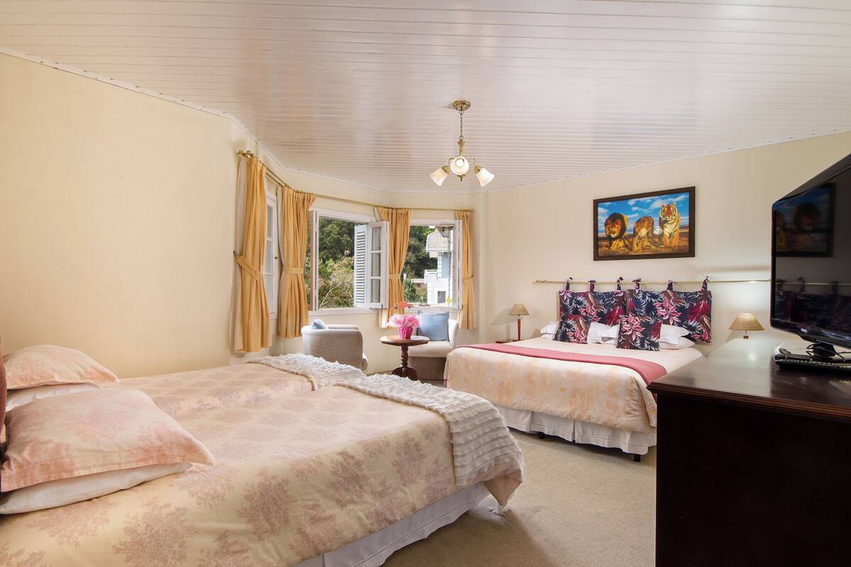 Habitación de hotel con dos camas, un escritorio, una silla, una ventana con cortinas, un cuadro y un ventilador de techo.