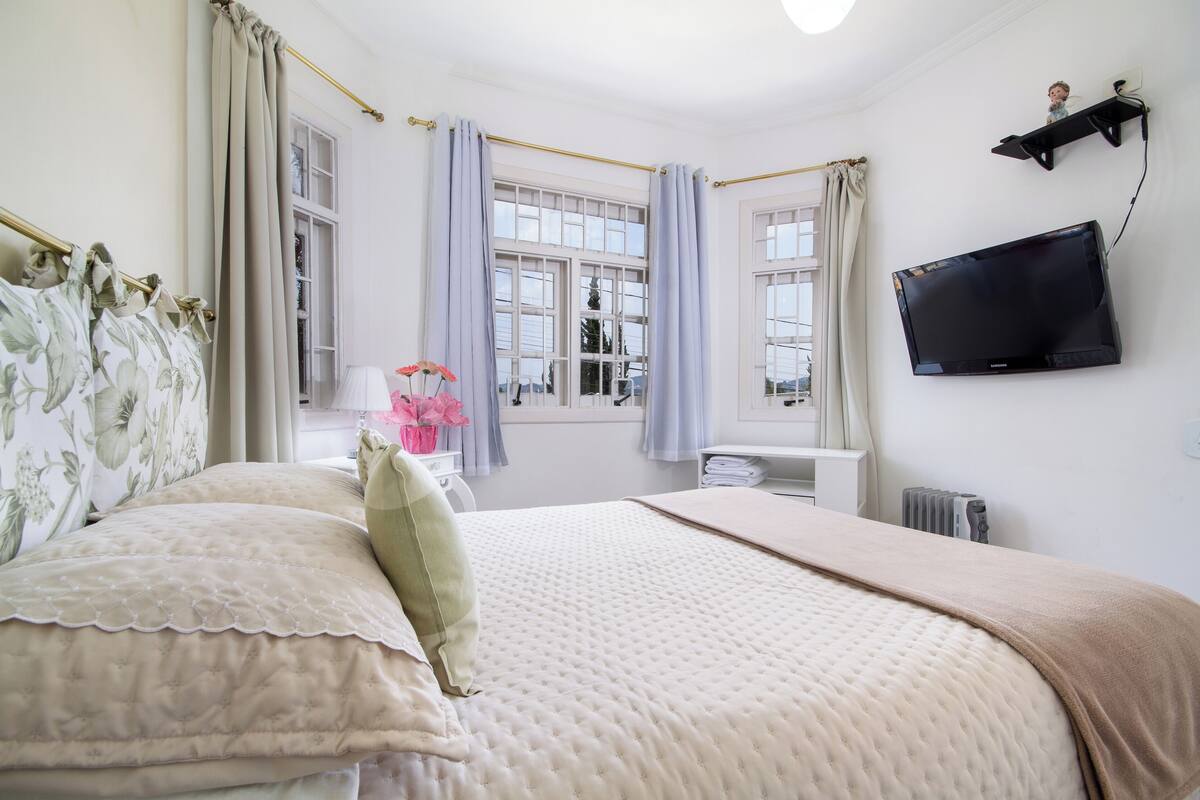 Un dormitorio con cama, cortinas, televisor y radiador.