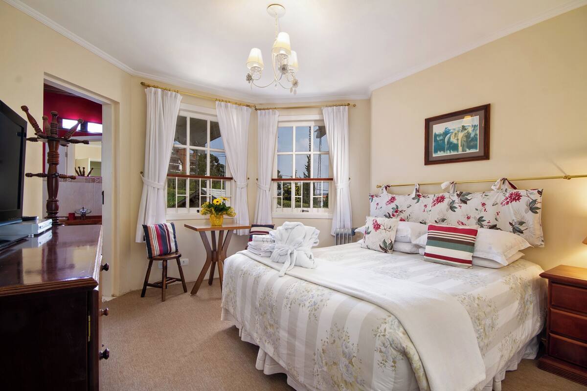 Un dormitorio con una cama grande, un escritorio con una silla, un televisor y una ventana con cortinas.