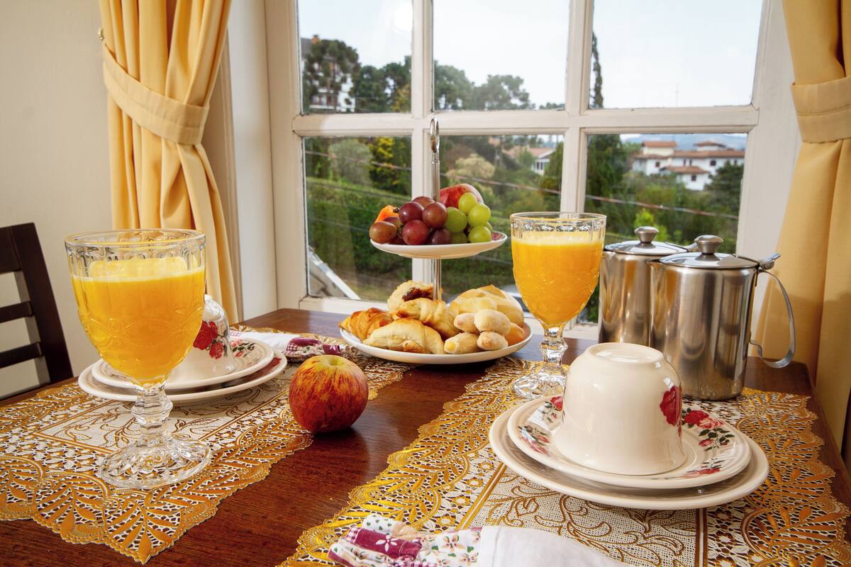 Una mesa de desayuno con una fuente de fruta, dos vasos de zumo de naranja, una tetera y una cafetera.