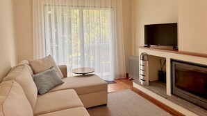 A modern living room with a beige sofa, a flat-screen TV, and a fireplace. - Casa dos Pais - Garden & Lake I (Ponta Delgada)