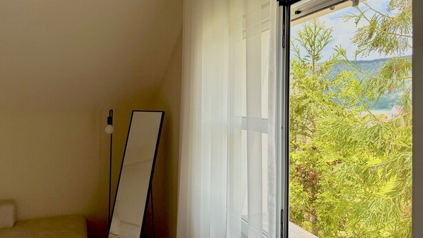 A room with a large window, a mirror, and a view of greenery and hills. - Casa dos Pais - Garden & Lake I (Ponta Delgada)