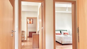 A hotel room with a wooden floor, a bed with white bedding, a dresser, a chair, and a desk. - Casa dos Avós - Garden & Lake II (Ponta Delgada)
