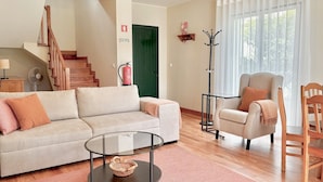 A living room with a sofa, armchair, and coffee table, a staircase, a green door, and a window with curtains. - Casa dos Avós - Garden & Lake II (Ponta Delgada)