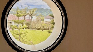 A circular window with a view of a residential area, including houses and greenery. - Casa dos Avós - Garden & Lake II (Ponta Delgada)
