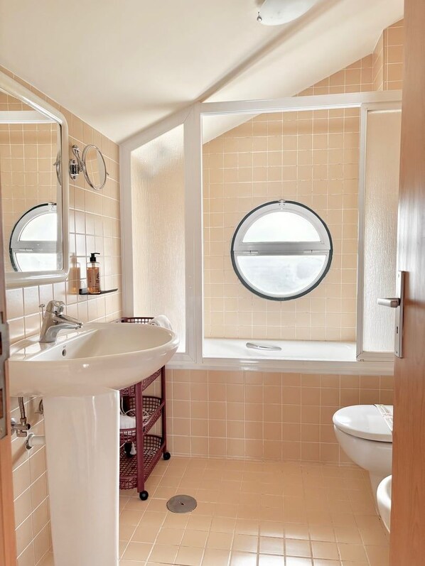 Un baño con un lavamanos grande, una ventana redonda y un inodoro.