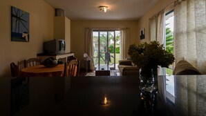 A dining area with a table, chairs, and a television. There is a sliding glass door leading to a balcony with a bicycle. - Casa dos Netos - Garden & Lake III (Ponta Delgada)