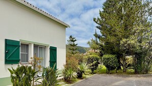 A residential building with a white exterior and green shutters, surrounded by lush greenery and a clear sky. - Casa dos Netos - Garden & Lake III (Ponta Delgada)